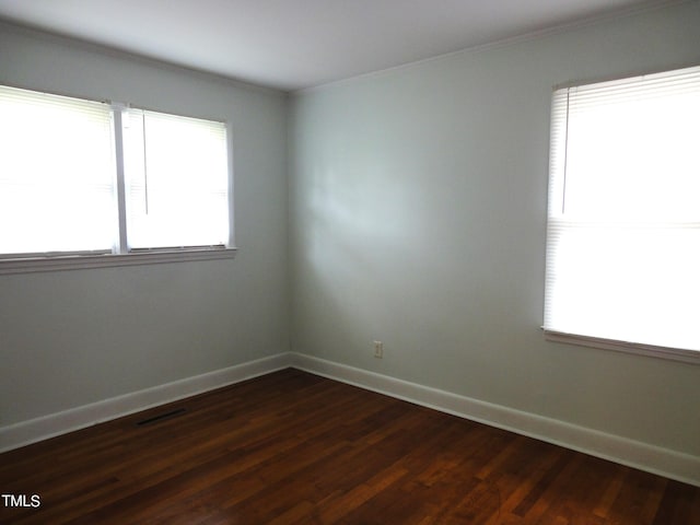 spare room featuring crown molding, dark wood-style floors, baseboards, and visible vents