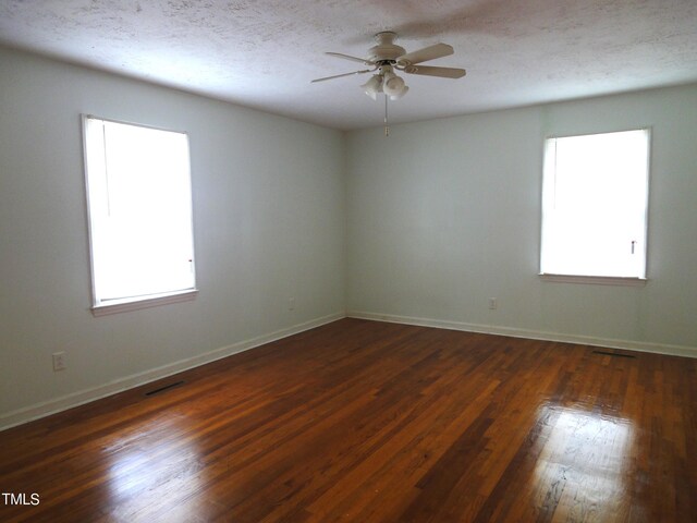 empty room featuring dark wood-style flooring, a textured ceiling, a ceiling fan, and plenty of natural light