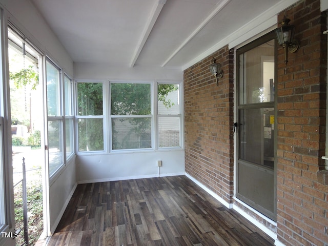 unfurnished sunroom featuring a wealth of natural light, wood finished floors, baseboards, and brick wall