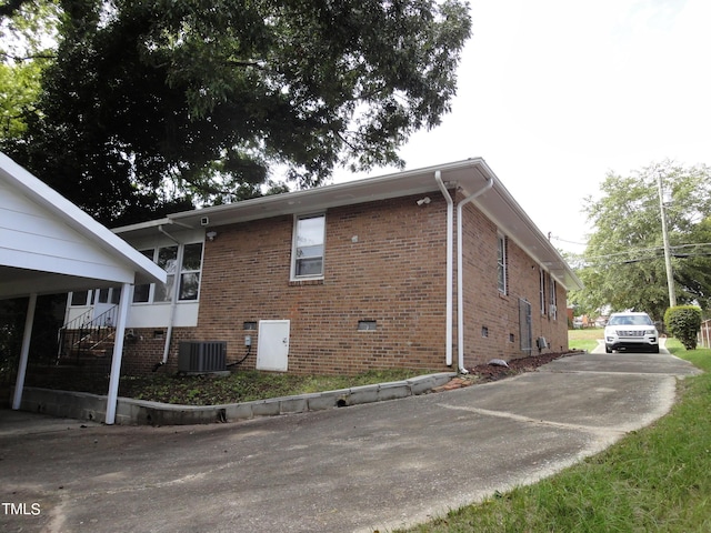 view of property exterior with central AC unit, driveway, and brick siding