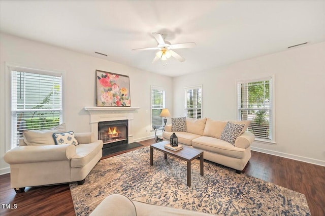 living area with a fireplace with flush hearth, baseboards, dark wood-style floors, visible vents, and ceiling fan