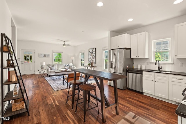 kitchen featuring appliances with stainless steel finishes, a sink, dark countertops, white cabinets, and dark wood-style floors