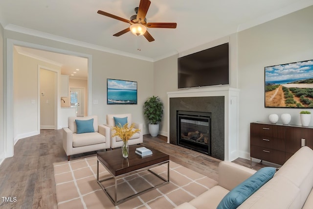living room with ornamental molding, baseboards, ceiling fan, a glass covered fireplace, and wood finished floors