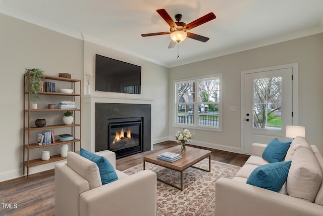 living room with plenty of natural light, crown molding, wood finished floors, and a glass covered fireplace