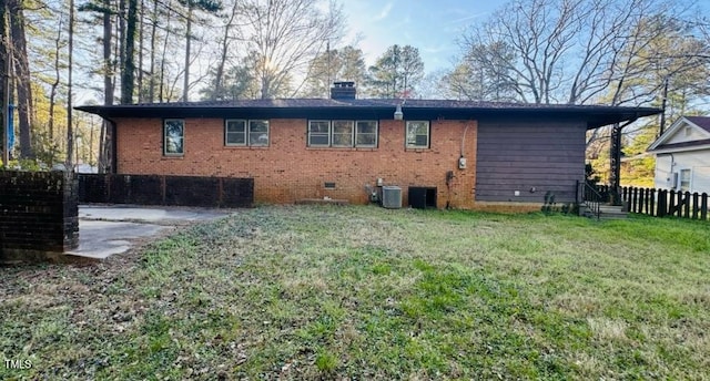 back of house featuring brick siding, a lawn, fence, and a chimney