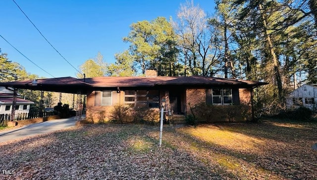 ranch-style home featuring driveway, a carport, a chimney, and brick siding