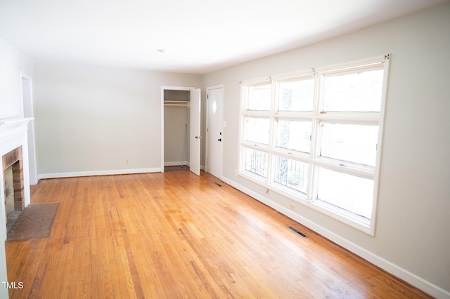 1115 Park Ave, Henderson, NC 27536 - unfurnished living room featuring light wood-type flooring, a brick fireplace, and plenty of natural light