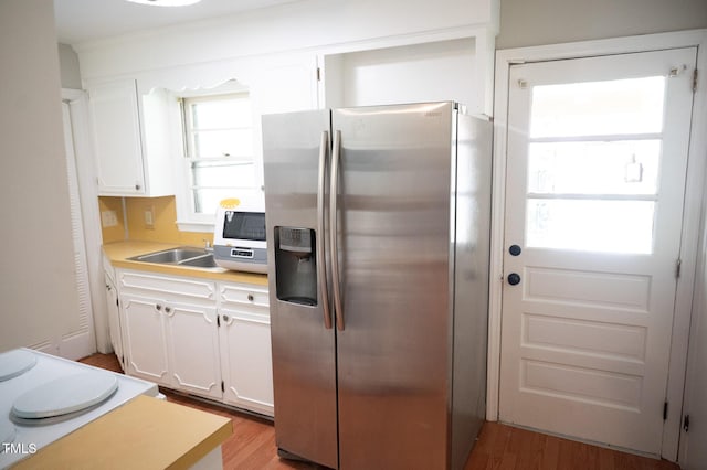 1115 Park Ave, Henderson, NC 27536 - kitchen featuring stainless steel fridge, light wood-type flooring, white cabinetry, and light countertops