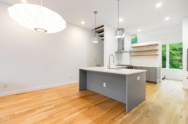 kitchen with open shelves, a sink, gray cabinetry, wall chimney range hood, and light wood-type flooring