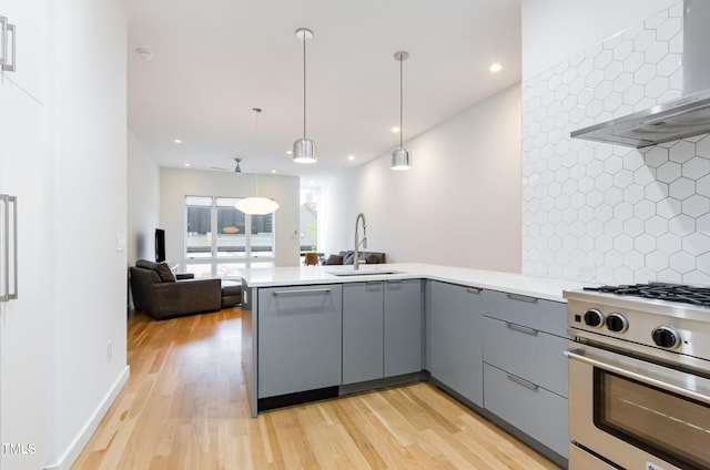 kitchen with stainless steel appliances, gray cabinets, a sink, a peninsula, and wall chimney range hood