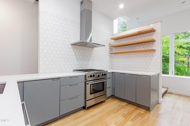 kitchen with gray cabinets, high end stove, wall chimney exhaust hood, and healthy amount of natural light