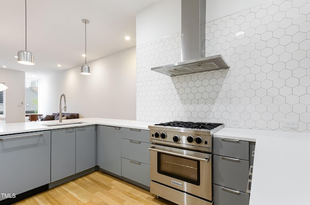 kitchen featuring appliances with stainless steel finishes, wall chimney range hood, gray cabinetry, a sink, and backsplash