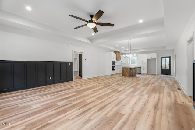 unfurnished living room with light wood-style flooring, ceiling fan with notable chandelier, baseboards, and recessed lighting