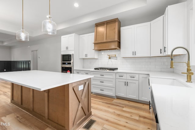 kitchen featuring visible vents, tasteful backsplash, a sink, light wood-style floors, and custom range hood