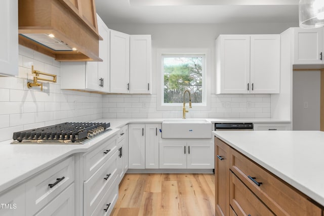 kitchen featuring light countertops, stainless steel gas cooktop, premium range hood, a sink, and light wood-style floors