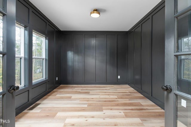 spare room featuring light wood-style flooring, a decorative wall, and visible vents