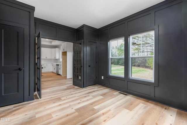 foyer entrance featuring a decorative wall, light wood finished floors, and visible vents
