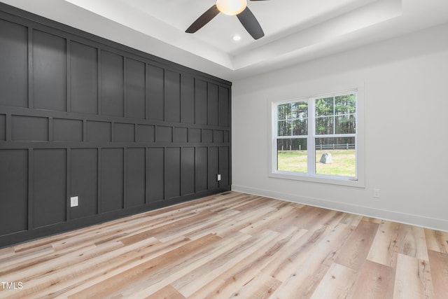 empty room featuring a tray ceiling, a decorative wall, light wood-style floors, and a ceiling fan