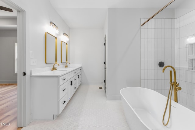 bathroom featuring a soaking tub, double vanity, a sink, and baseboards