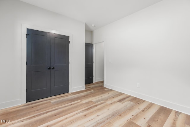 unfurnished bedroom featuring baseboards, light wood-style flooring, and a closet