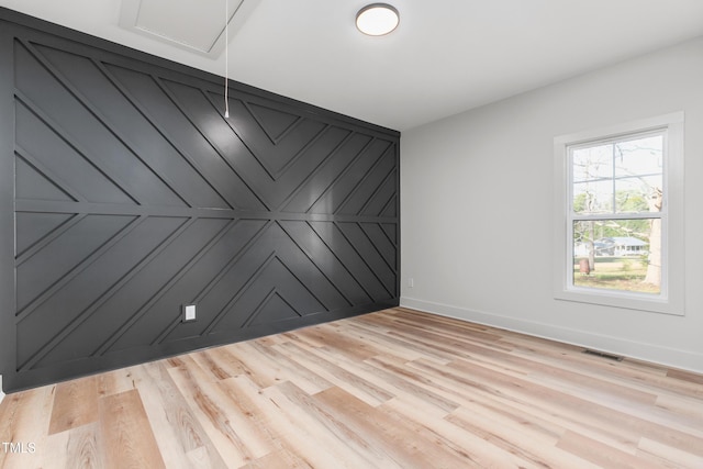 unfurnished room featuring baseboards, visible vents, an accent wall, and light wood-type flooring