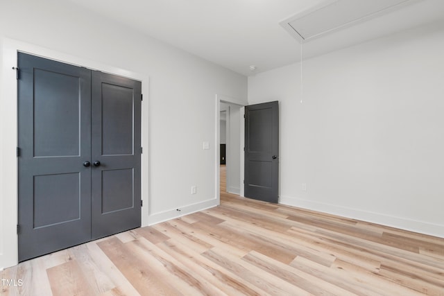 unfurnished bedroom featuring a closet, baseboards, attic access, and light wood-type flooring