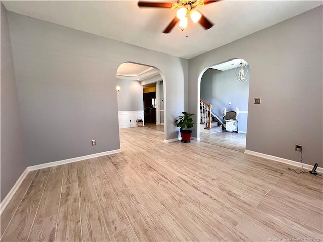 spare room featuring ceiling fan, light wood finished floors, arched walkways, and baseboards