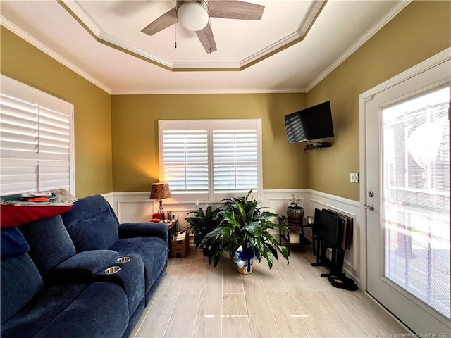 living room with wainscoting, ceiling fan, ornamental molding, and a raised ceiling