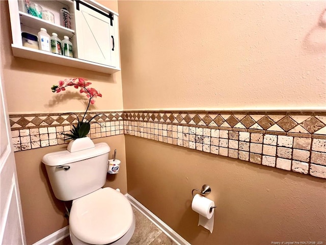 bathroom featuring a wainscoted wall, tile walls, and toilet