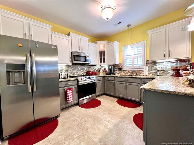 kitchen with light stone countertops, visible vents, decorative backsplash, stainless steel appliances, and hanging light fixtures