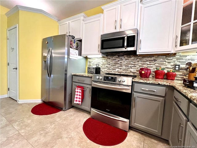 kitchen featuring glass insert cabinets, backsplash, gray cabinetry, light stone countertops, and stainless steel appliances