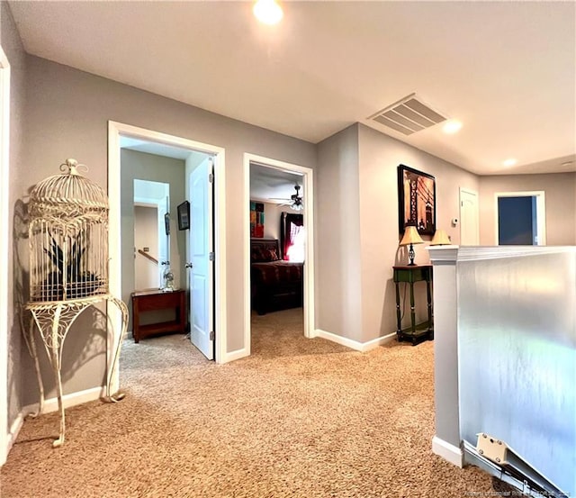 hall with visible vents, baseboards, and light carpet