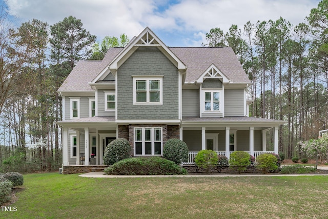 craftsman-style house featuring a front yard, roof with shingles, stone siding, and covered porch