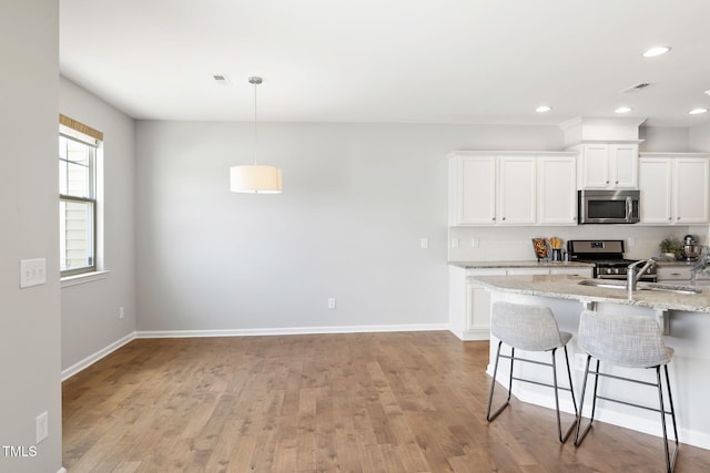 122 Torpoint Rd, Durham, NC 27703 - kitchen featuring appliances with stainless steel finishes, a breakfast bar, white cabinetry, light wood-style floors, and recessed lighting