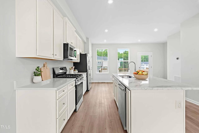 609 Silverado Sunset Loop, Wendell, NC 27591 - kitchen featuring stainless steel appliances, a sink, white cabinetry, a center island with sink, and light wood-style floors