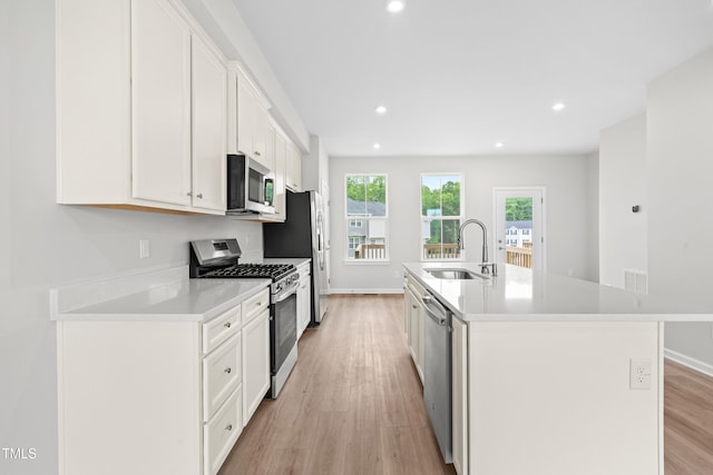 609 Silverado Sunset Loop, Wendell, NC 27591 - kitchen featuring stainless steel appliances, a sink, white cabinetry, light wood-style floors, and an island with sink