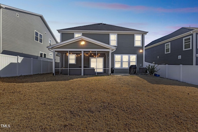 rear view of property featuring a fenced backyard, a sunroom, and a yard
