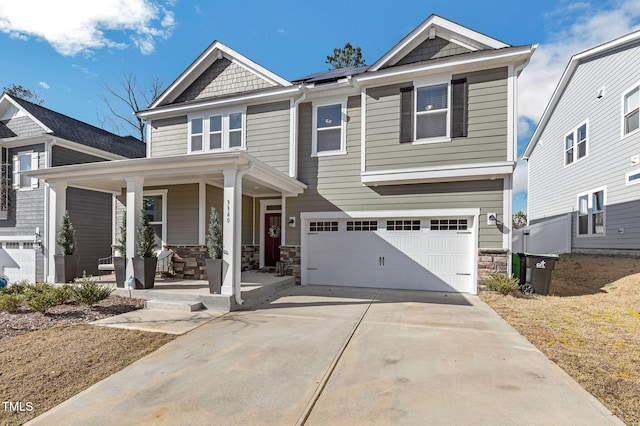 craftsman inspired home with stone siding, roof mounted solar panels, a garage, driveway, and a porch