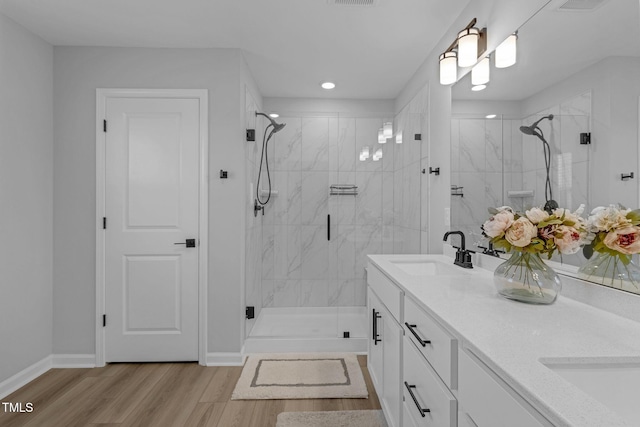 bathroom featuring double vanity, a sink, a marble finish shower, and wood finished floors