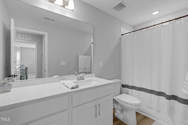 bathroom with toilet, vanity, wood finished floors, and visible vents