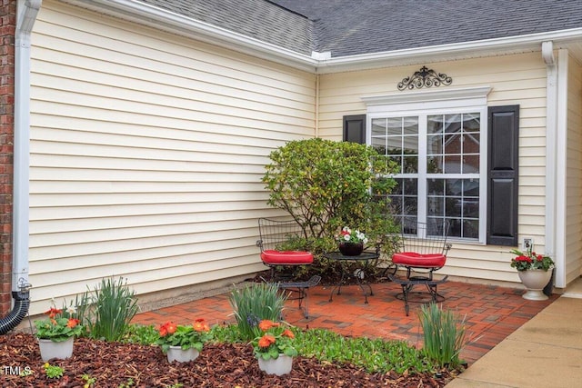 view of exterior entry with a patio and roof with shingles