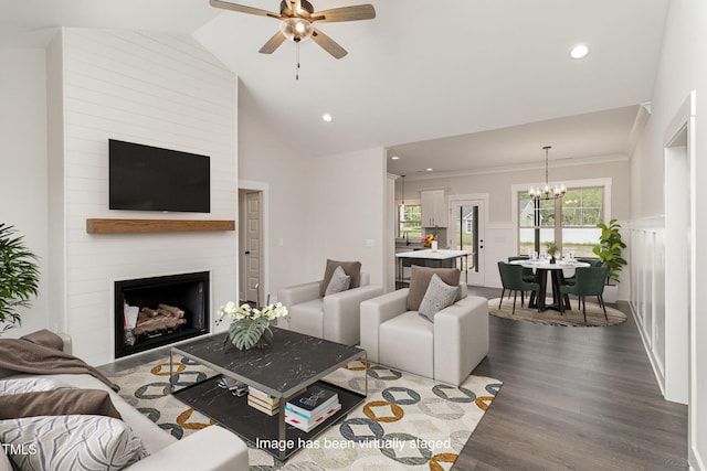 living area featuring a large fireplace, dark wood-type flooring, wainscoting, lofted ceiling, and ceiling fan with notable chandelier