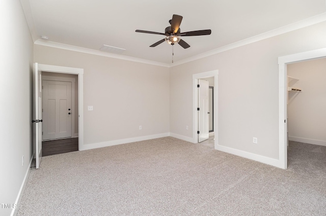unfurnished bedroom with baseboards, ornamental molding, carpet floors, a walk in closet, and ceiling fan