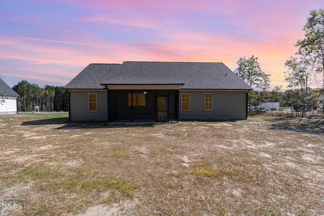 back of house at dusk featuring a shingled roof and a sunroom