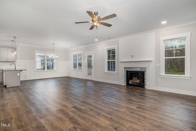 unfurnished living room with crown molding, ceiling fan with notable chandelier, a fireplace, dark wood finished floors, and a sink