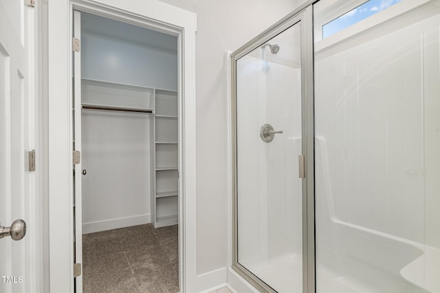 bathroom featuring a spacious closet, a shower stall, and baseboards