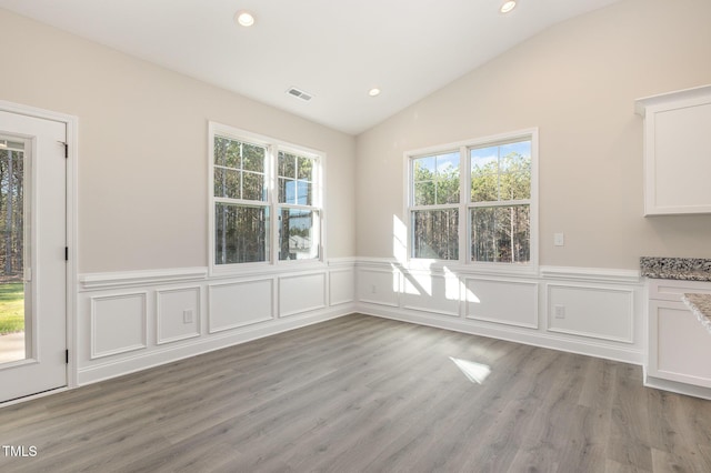 unfurnished dining area with light wood-style floors, visible vents, vaulted ceiling, recessed lighting, and wainscoting