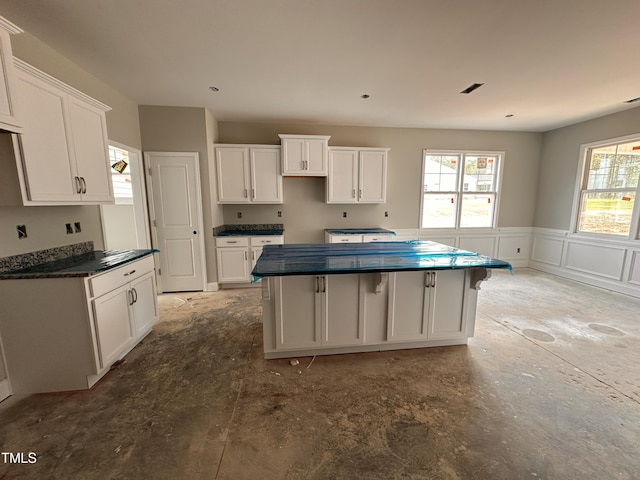 kitchen featuring wainscoting, dark countertops, a center island, and white cabinetry