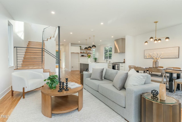 living room featuring stairway, recessed lighting, an inviting chandelier, baseboards, and light wood-style floors