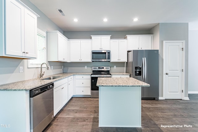 kitchen featuring appliances with stainless steel finishes, a sink, a kitchen island, dark wood-type flooring, and white cabinetry